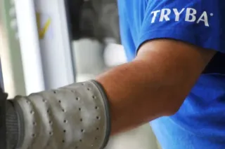 TRYBA_Suisse_Formation_partenaire.webp Un employé portant un t-shirt bleu 'TRYBA' travaille avec des gants protecteurs sur une installation.