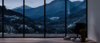 TRYBA_Suisse.webp Vue imprenable sur des montagnes couvertes de forêts enneigées, encadrées par de grandes baies vitrées d'un intérieur moderne et
