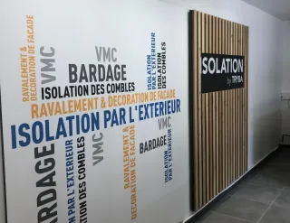 visuel_bloc_1.webp Une image montrant un mur avec des mots-clés sur l'isolation et le bardage entourant une partie en bois portant le logo 'Isolation
