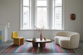 vitrage_isolation_phonique.webp Un salon moderne lumineux avec des meubles contemporains, comprenant une table basse en bois, une chaise jaune, un canapé blanc et un tapis rayé color