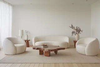 vitrage_isolation_thermique.webp Un salon moderne et minimaliste avec un mobilier blanc incurvé et une table en bois naturel sur un tapis clair.