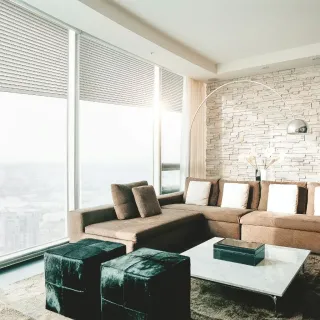 volet_isolation.webp Un salon moderne et élégant avec un canapé d'angle marron, des poufs noirs, une table basse en marbre et un mur en pierre