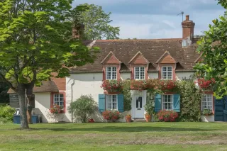 volet_quel_volet_situation.webp Une charmante maison de campagne avec des volets bleus et des fleurs colorées ornant la façade.
